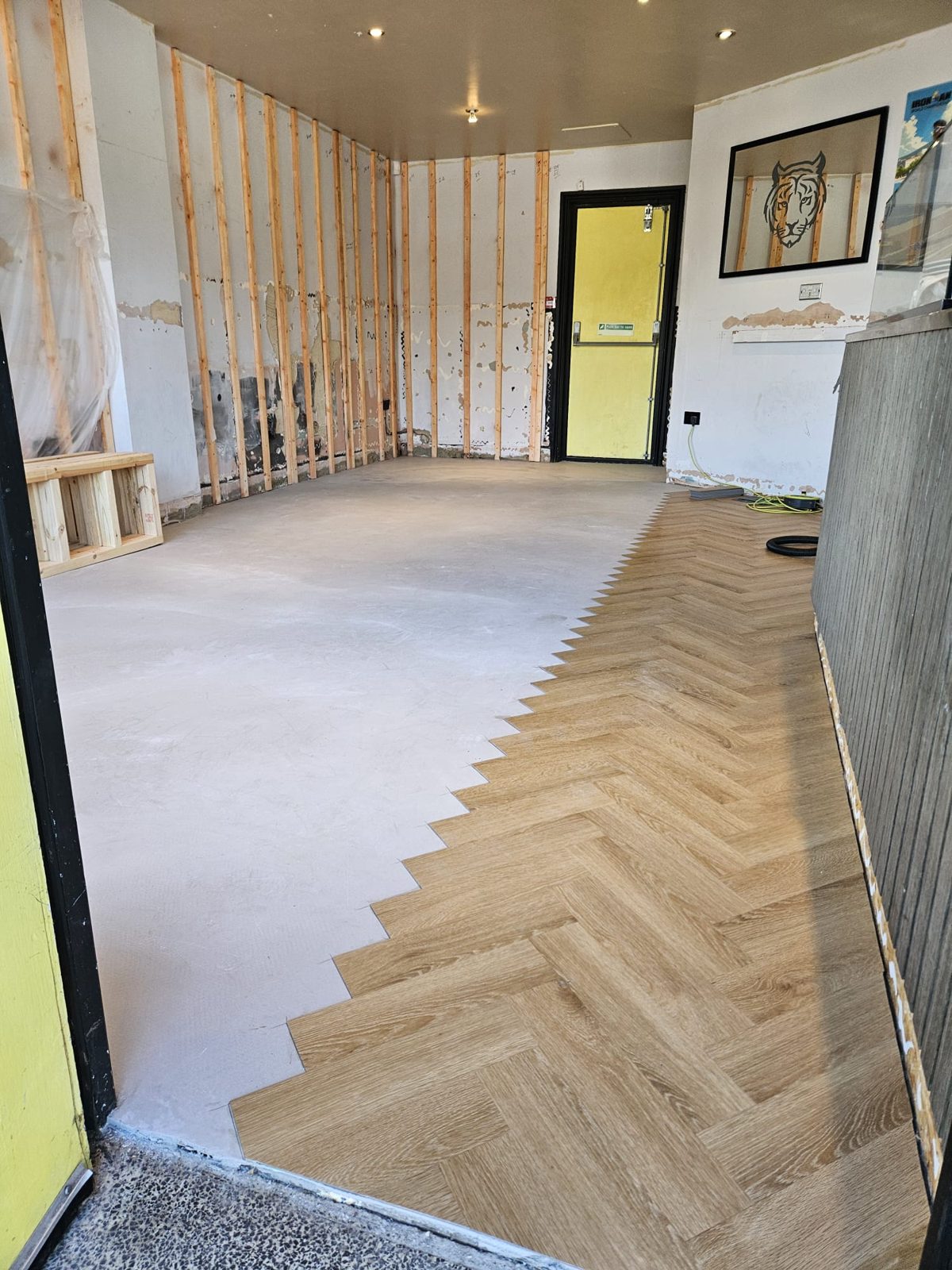 Herringbone LVT planks half laid across the smooth screed
