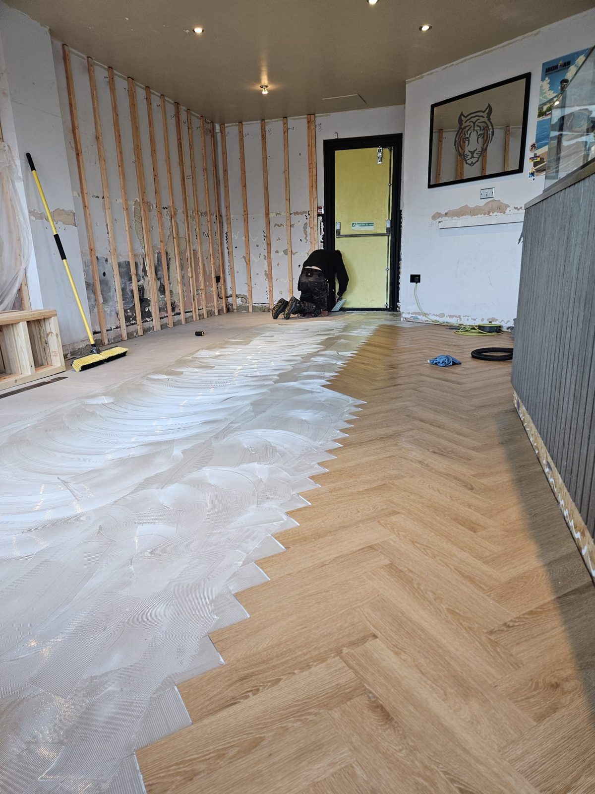 Uzin adhesive trowelled onto the screed beside newly laid herringbone LVT